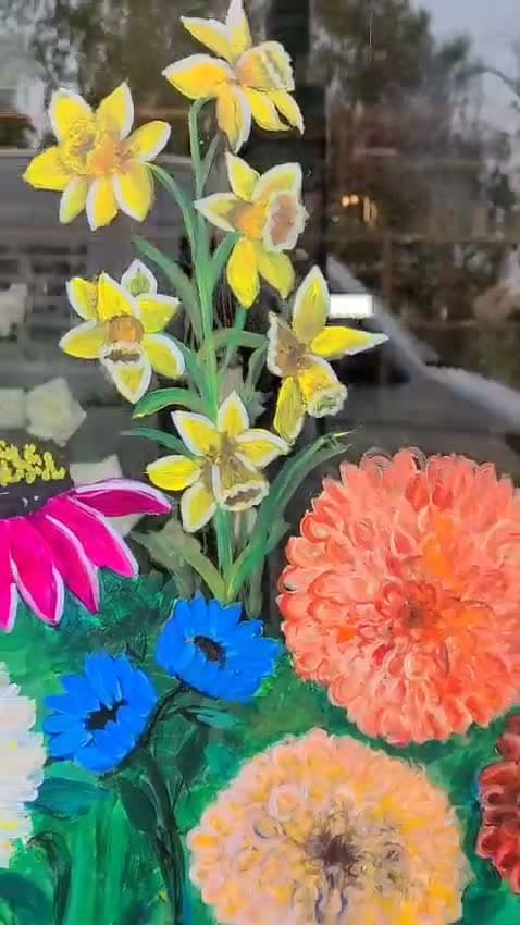 Daffodils painted on glass being finished with white highlights, above magenta echinacea and orange dahlias.