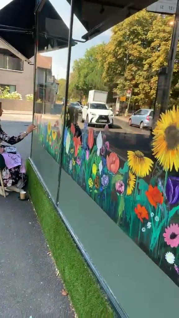 A hand-painted wildflower mural running the length of a florist's shopfront glazing — sunflowers, delphiniums and poppies, with the street reflected in the glass above.